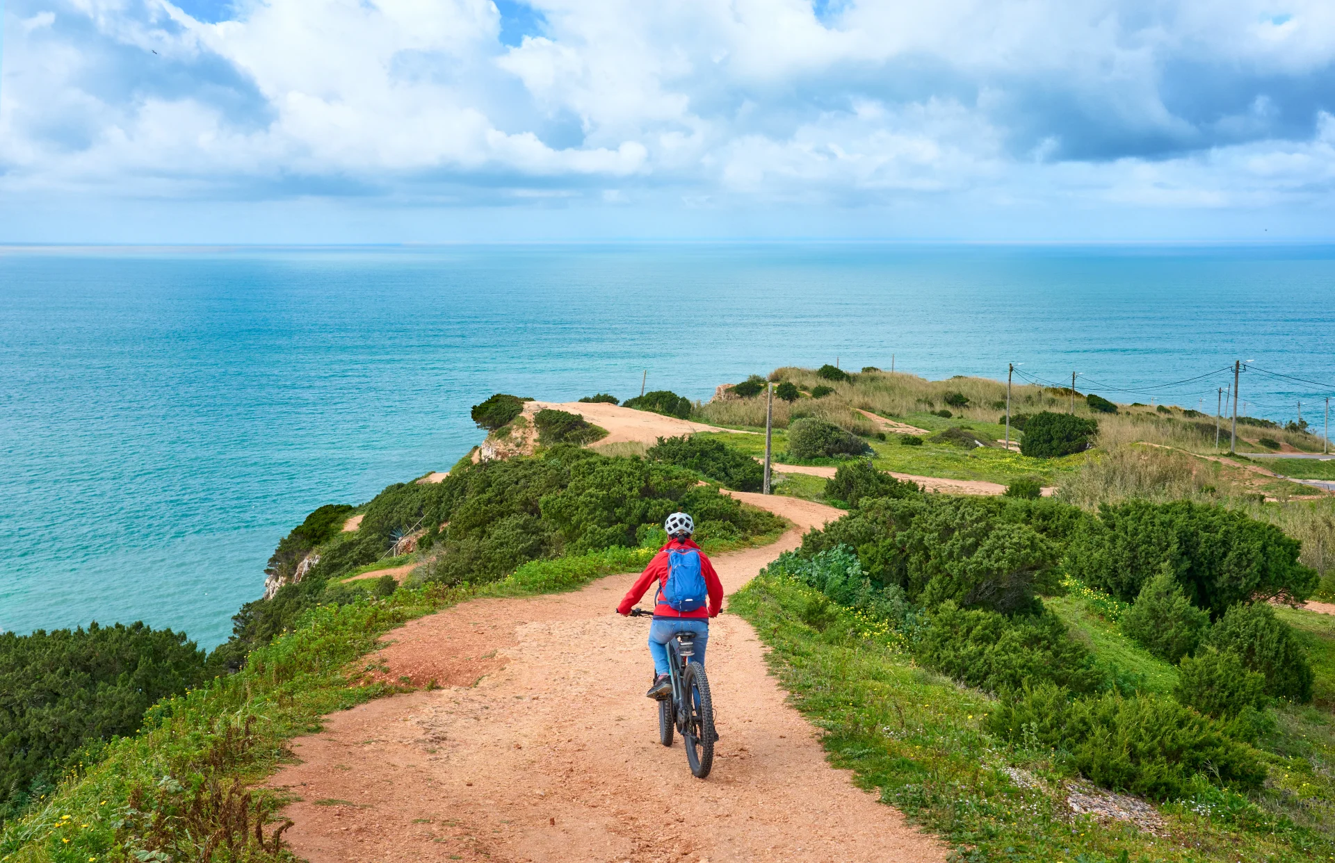 nice-senior-woman-riding-her-electric-mountain-bike-on-the-rocky-cliffs-of-nazare-at-the-western-atlantic-coast-of-portugal